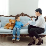 A calm, professional clinic setting with a parent and child speaking with a clinician about psychological testing, with subtle educational materials nearby.