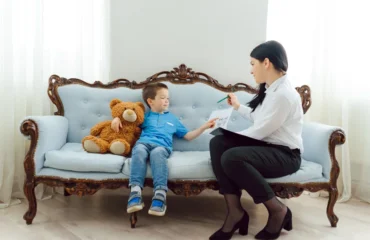 psychological-testing-kids-teens-signs-evaluation-involves A calm, professional clinic setting with a parent and child speaking with a clinician about psychological testing, with subtle educational materials nearby.
